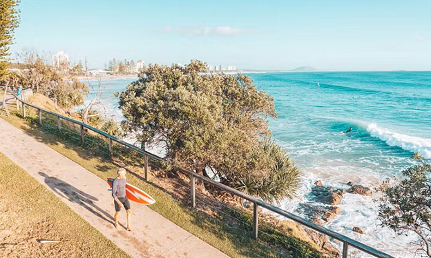 Man with surfboard walking on the sidewalk overlooking the ocean on Sunshine Coast, Queensland